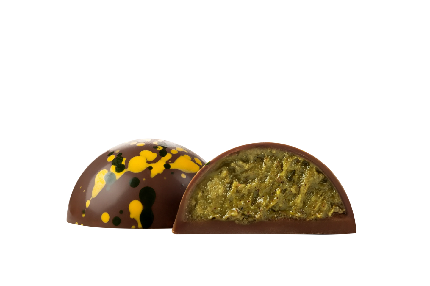 Дві круглі Цукерки Millennium CRAFT Dubai Chocolate від Millennium, одна ціла з жовтими та зеленими бризками, інша розрізана навпіл, щоб відкрити зелену фісташкову начинку, зображену на білому тлі.