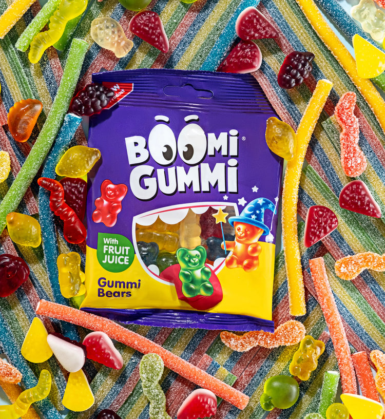 Фіолетовий мішечок для цукерок Boomi Gummi Gummi Bears на смугастій поверхні, оточений різнокольоровими жувальними цукерками та кислими смужками.