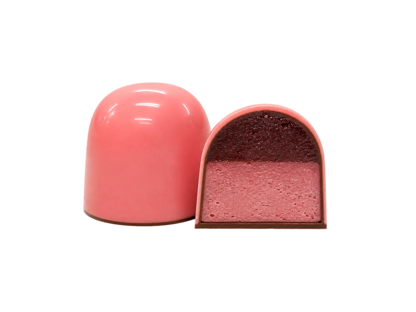 На фото зображено дві куполоподібні рожеві цукерки «Millennium Craft Raspberry Ganache with Stevia» від Millennium Chocolate — одна ціла, а інша розрізана навпіл, щоб можна було побачити їх багатошарову структуру з глянцевою рожевою глазур’ю. Всередині ви знайдете ніжні шари малинового мармеладу та малинового ганашу, що створюють чудовий контраст смаків.