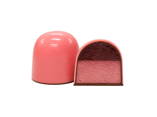 На фото зображено дві куполоподібні рожеві цукерки «Millennium Craft Raspberry Ganache with Stevia» від Millennium Chocolate — одна ціла, а інша розрізана навпіл, щоб можна було побачити їх багатошарову структуру з глянцевою рожевою глазур’ю. Всередині ви знайдете ніжні шари малинового мармеладу та малинового ганашу, що створюють чудовий контраст смаків.