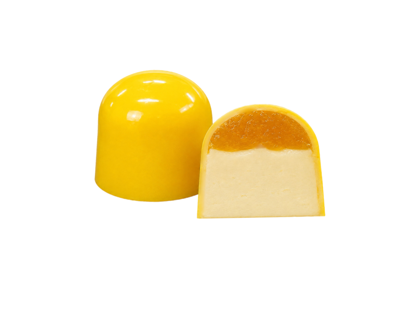 Дві жовті цукерки у формі купола «Millennium Craft Mango & Coconut with Stevia» від Millennium Chocolate виготовлені з білого шоколаду. Одна з них ціла, а інша розрізана навпіл, щоб було видно кремово-білу начинку з кокосового пюре, покриту яскравим шаром мангового мармеладу. Обидві цукерки розміщені на однотонному білому тлі.